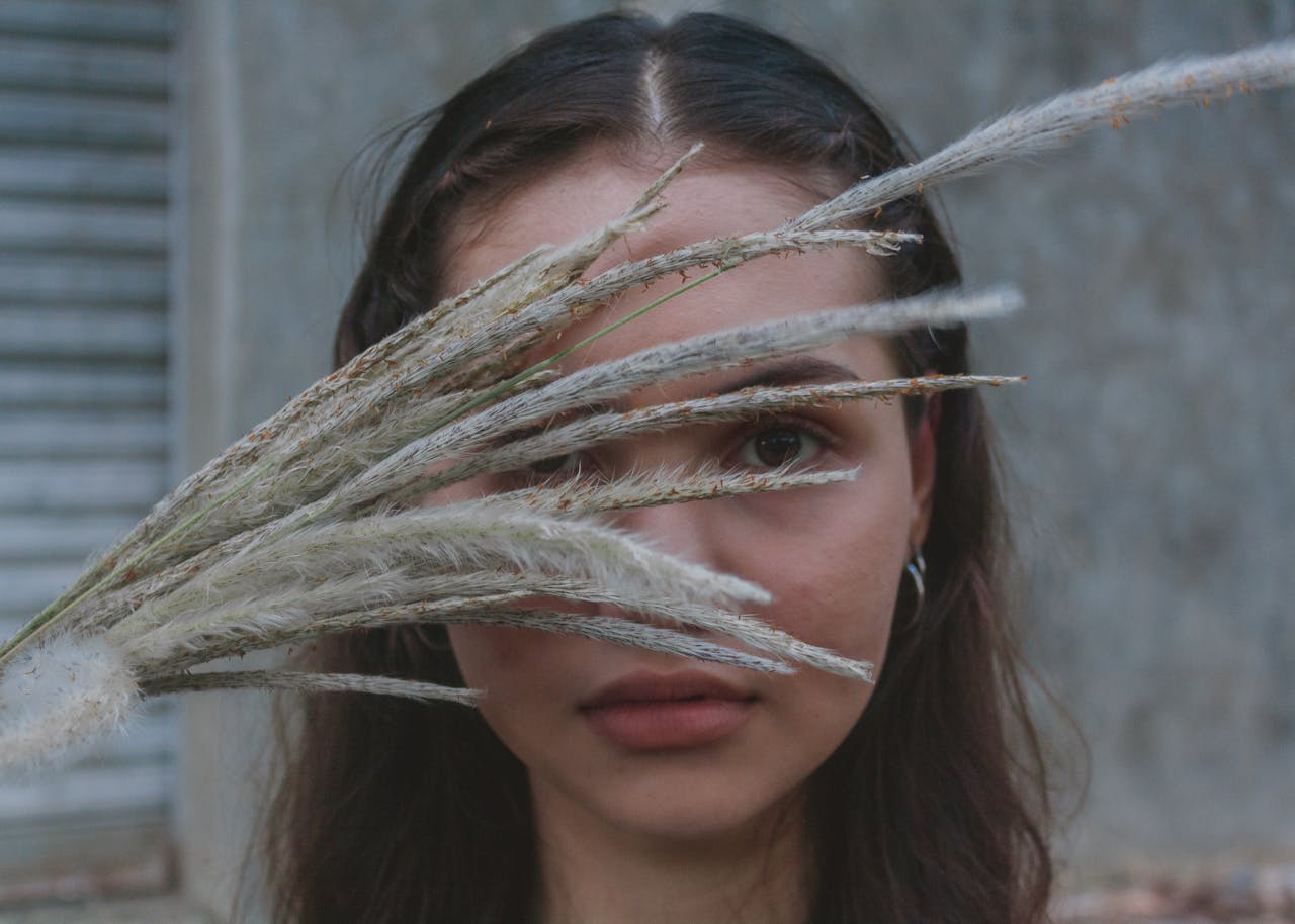 Artistic portrait of a woman with grass stalks obscuring her face, creating a mysterious and serene mood.